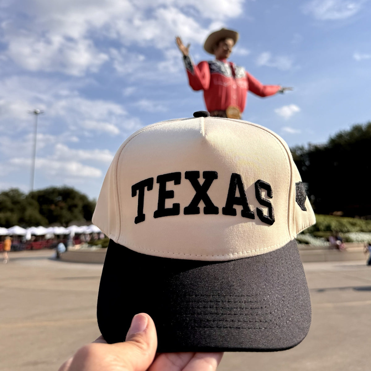 Texas Varsity trucker hat in Natural / Black Bill with raised black TEXAS block letters, held up at the State Fair of Texas