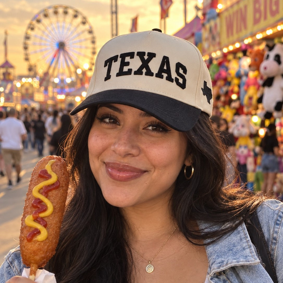 Woman at a fair midway wearing the Texas Varsity trucker hat in Natural / Black Bill