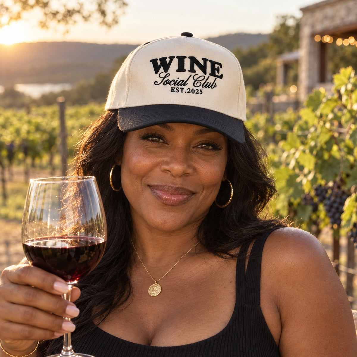 Woman in a Texas Hill Country vineyard holding red wine and wearing the Wine Social Club trucker hat in Natural / Black Bill