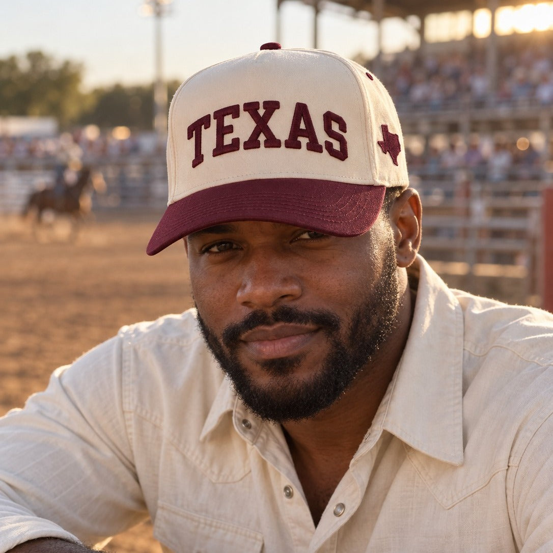 Man at a rodeo arena wearing the Texas Varsity trucker hat in Natural / Maroon Bill with matching maroon embroidery