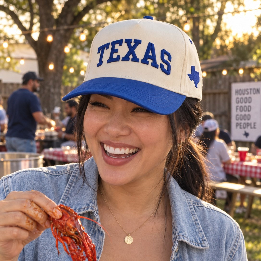 Woman at a Houston backyard crawfish boil wearing the Texas Varsity trucker hat in Natural / Royal Blue Bill with royal blue embroidery