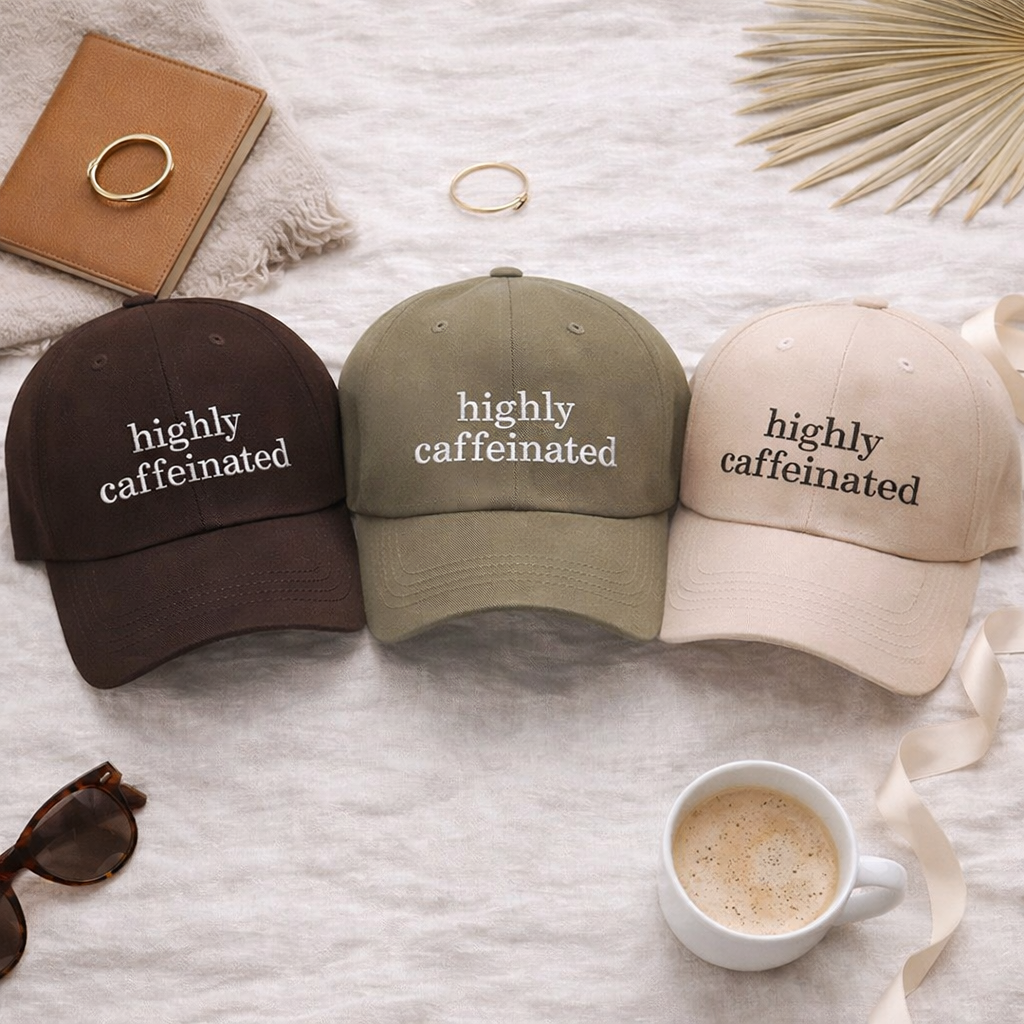 A close-up view of a flat lay of cotton baseball hats featuring the phrase Highly Caffeinated in bold, crisp white or black embroidery. - DSY Lifestyle