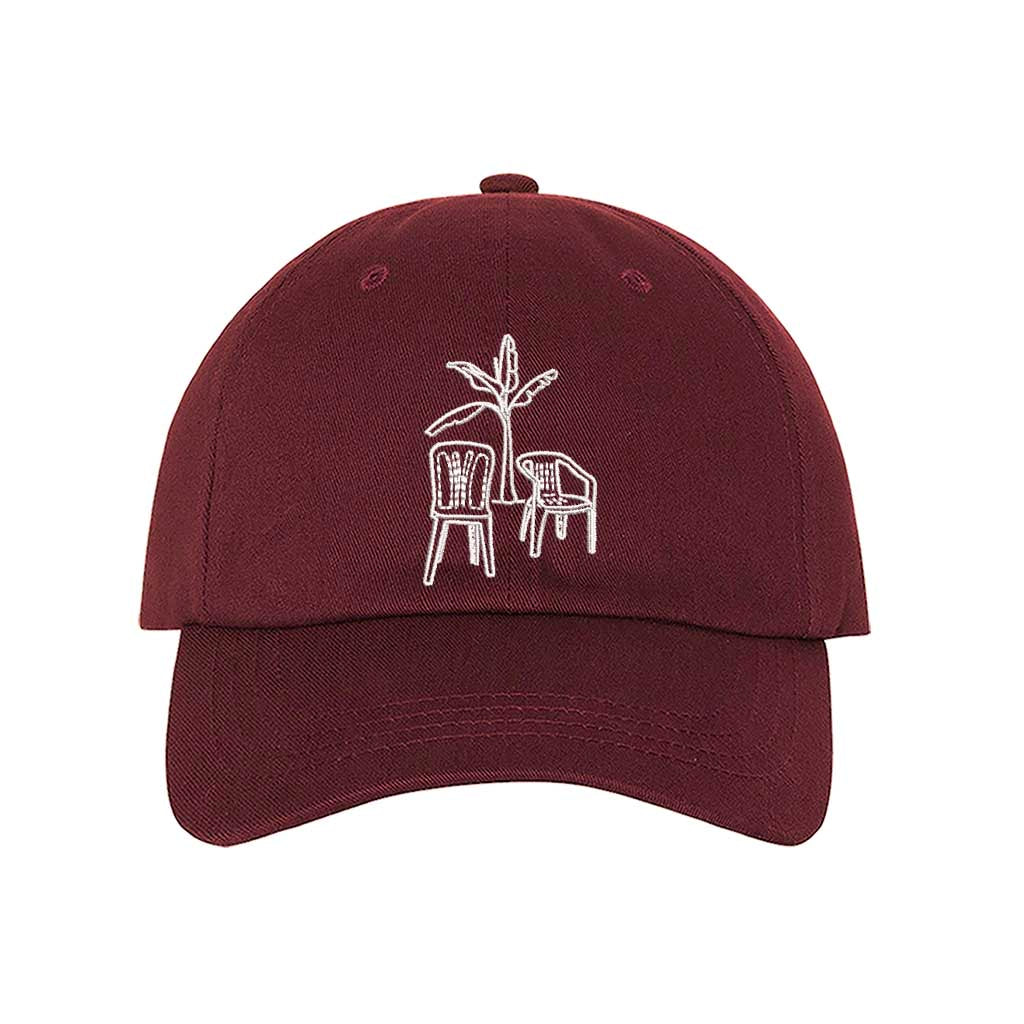 Front the DTMF Debi Tirar Mas Fotos burgundy dad cap featuring an embroidered banana tree with two chairs, inspired by Bad Bunny&