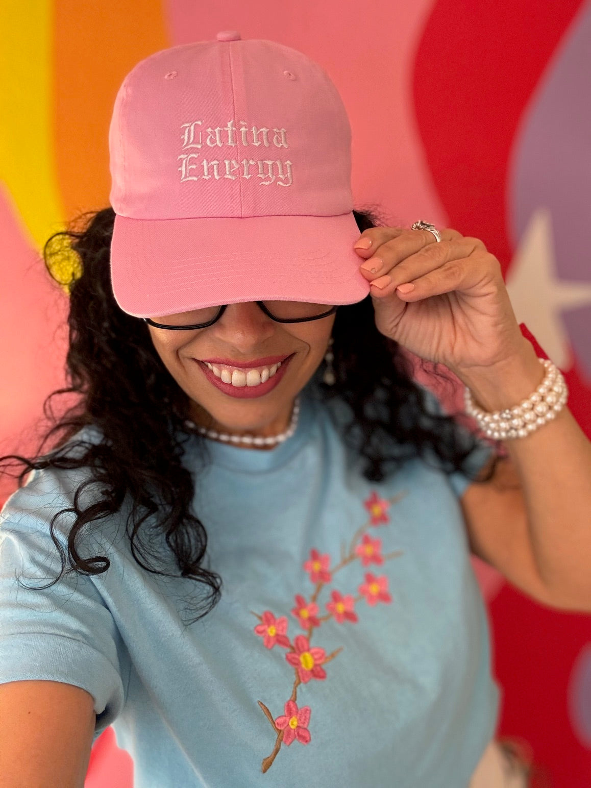 Lady wearing Light Pink baseball hat embroidered with the phrase Latina Energy in old English letters paired with a sky blue cherry blossom t-shirt-DSY Lifestyle