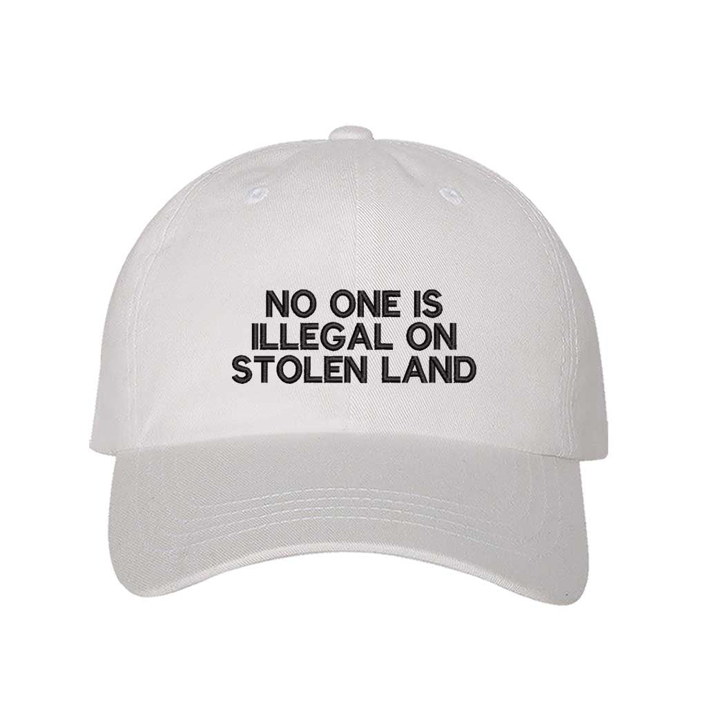 White No One Is Illegal On Stolen Land Baseball Hat featuring bold white embroidery on a classic cotton dad cap; a powerful social justice statement piece by DSY Lifestyle.