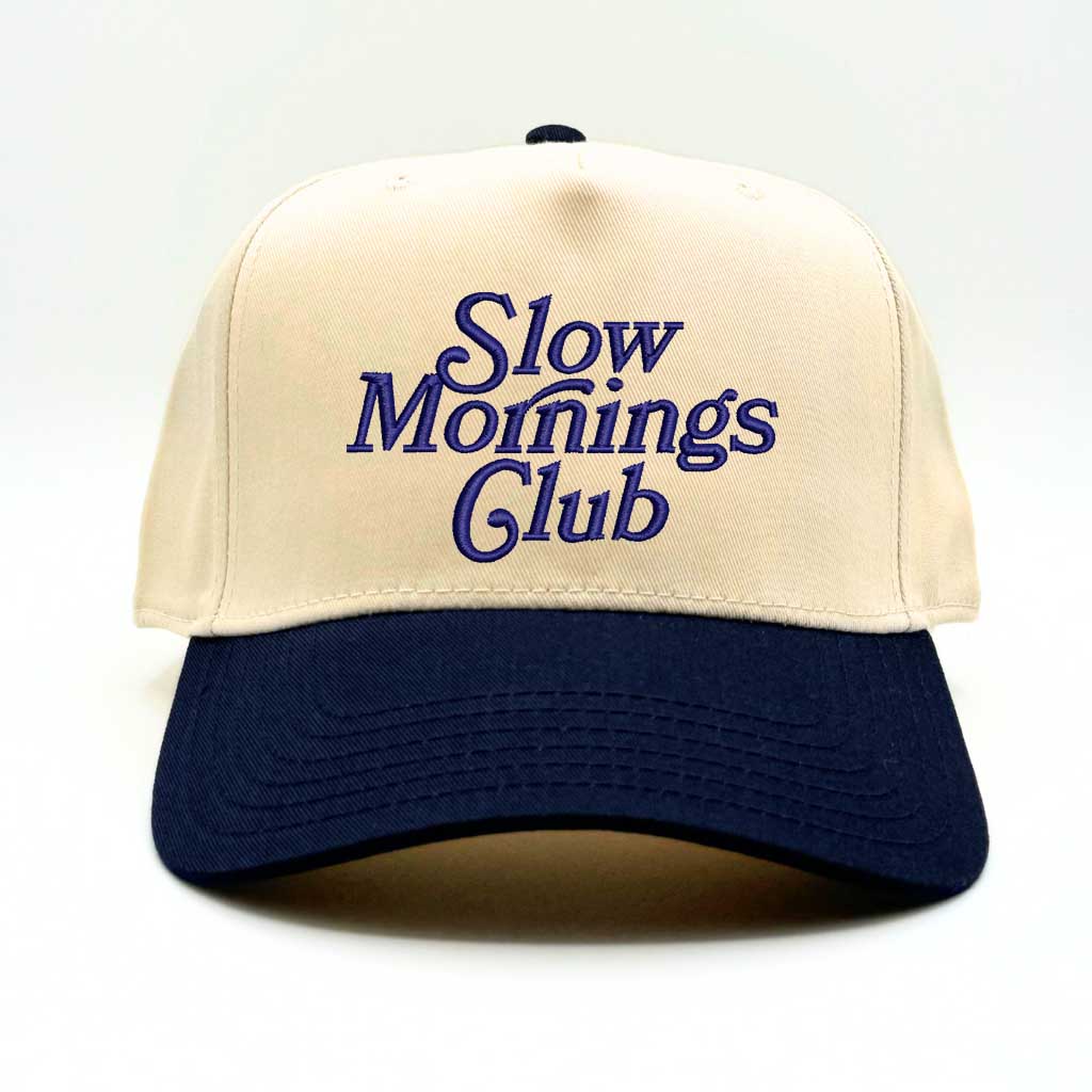 Beige and navy 5-panel baseball hat with "Slow Mornings Club" embroidered by DSY Lifestyle in navy on the front.