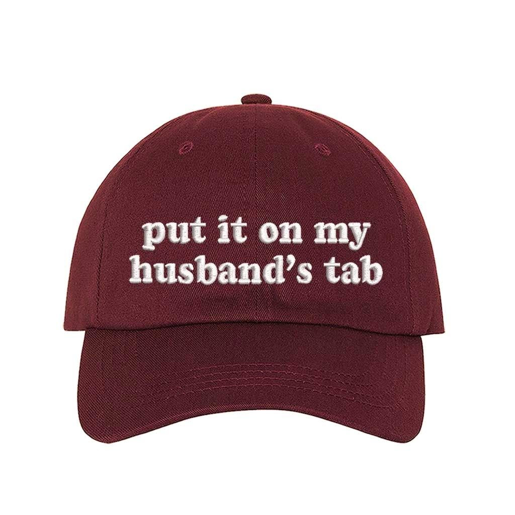 Burgundy Put It on My Husband’s Tab Embroidered Baseball Hat in soft cotton with curved brim and adjustable back strap, perfect for vacations and girls’ nights. DSY Lifestyle.