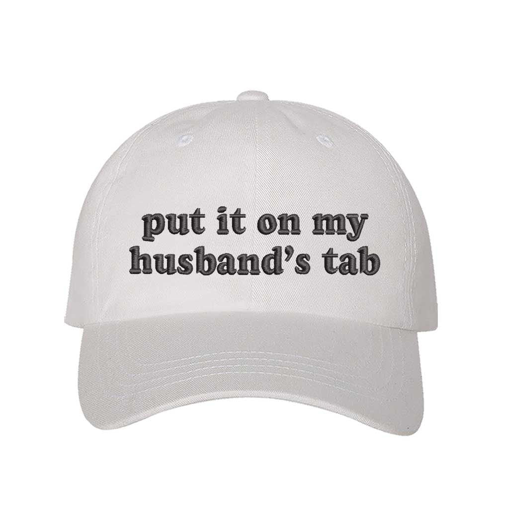 White Put It on My Husband’s Tab Embroidered Baseball Hat in soft cotton with curved brim and adjustable back strap, perfect for vacations and girls’ nights. DSY Lifestyle.