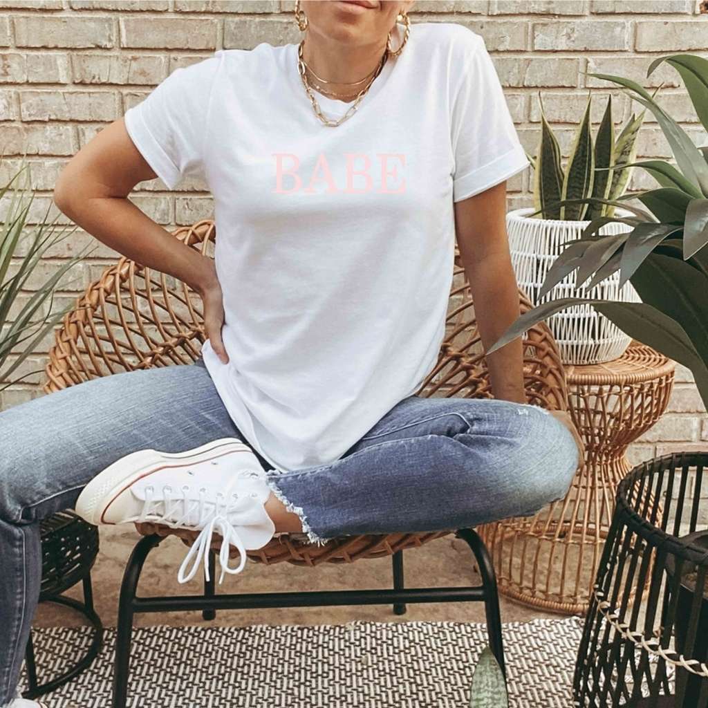 Female wearing a white unisex tshirt printed with BABE in pink - DSY Lifestyle