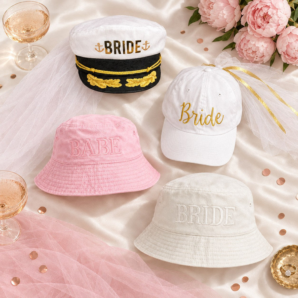 Flat lay of bachelorette party hats: white Bride captain hat with gold lettering, white Bride baseball hat with veil, pink BABE bucket hat and cream BRIDE bucket hat, with champagne coupes, peonies and tulle