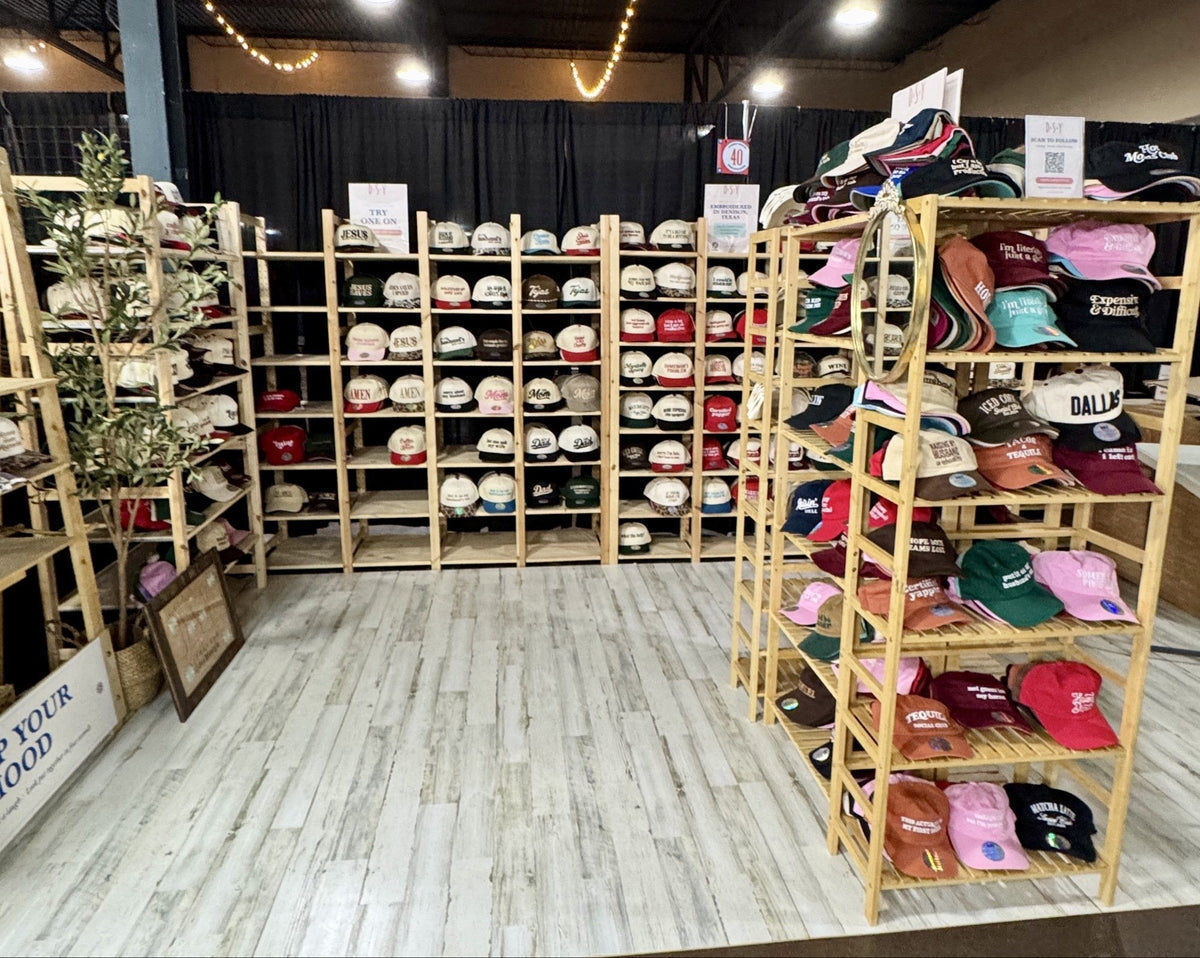 DSY Lifestyle embroidered hat booth, Space 40, Embarcadero Building at the 2026 State Fair of Texas, with wood shelves of hats on the new floor