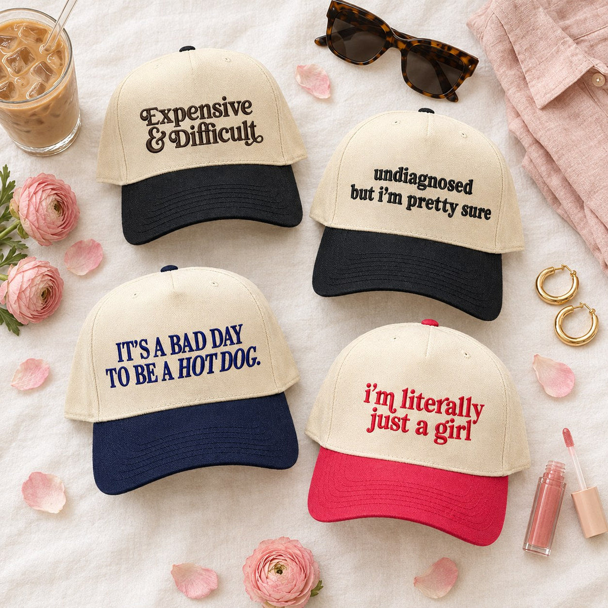 Flat lay of four funny embroidered trucker hats for women: Expensive & Difficult, undiagnosed but i'm pretty sure, It's a Bad Day to Be a Hot Dog and i'm literally just a girl, with an iced latte, sunglasses and pink flowers