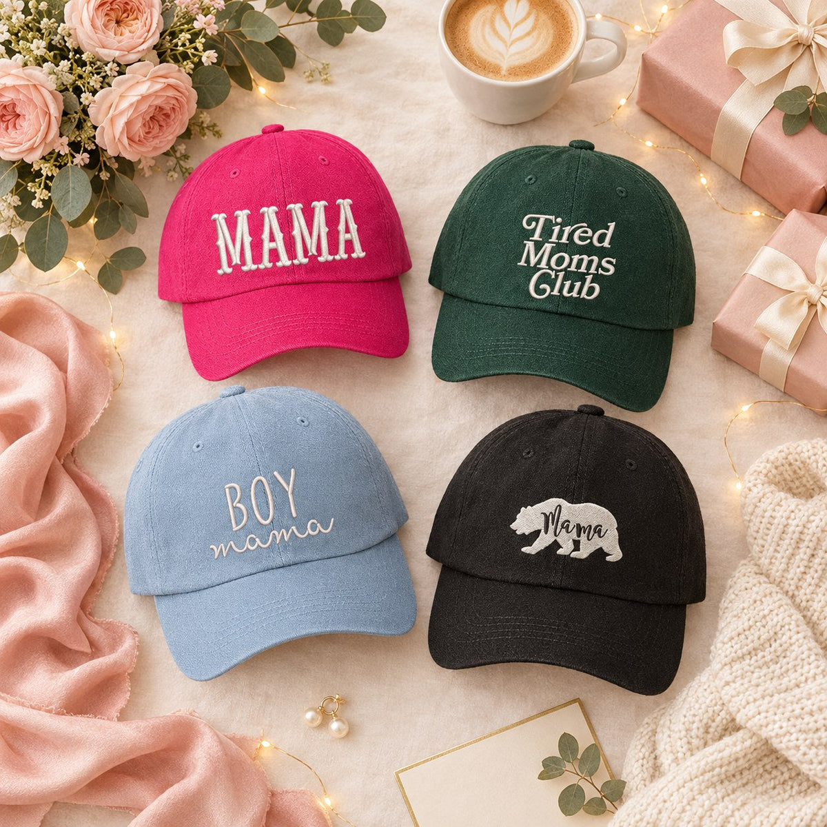 Flat lay of DSY embroidered gift hats for mom: hot pink Mama, Tired Moms Club, Boy Mama and Mama Bear baseball hats with roses, a latte and blush-wrapped gifts
