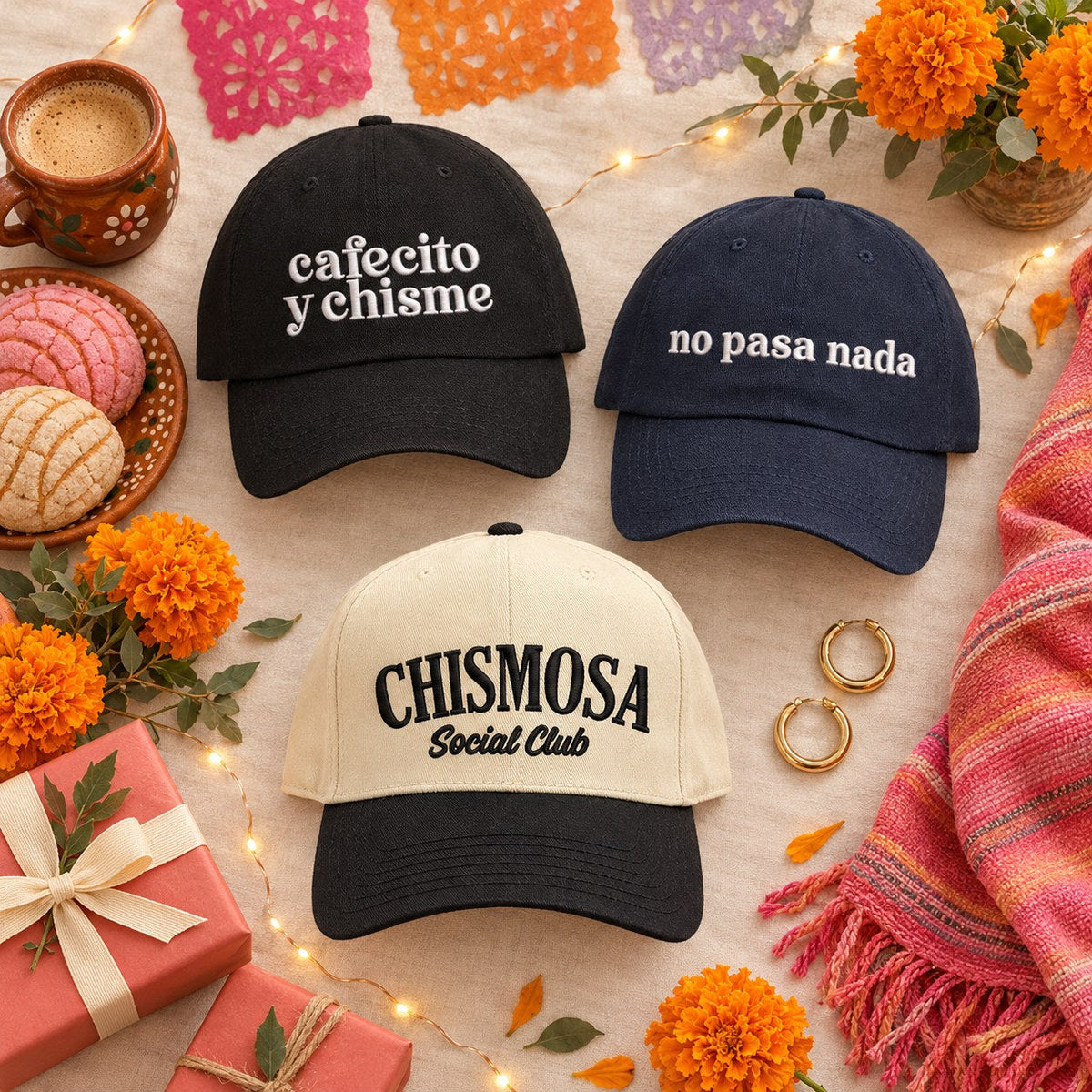 Flat lay of DSY embroidered Spanish-phrase hats for Latinas: Cafecito y Chisme, No Pasa Nada and Chismosa Social Club with cafecito, pan dulce conchas, marigolds and a woven rebozo