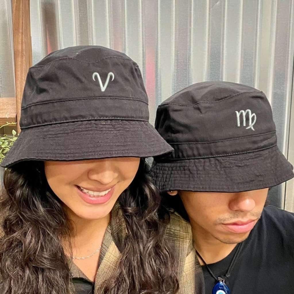 Female wearing a black bucket hat embroidered with aries. Male wearing a black bucket hat embroidered with virgo DSY Lifestyle