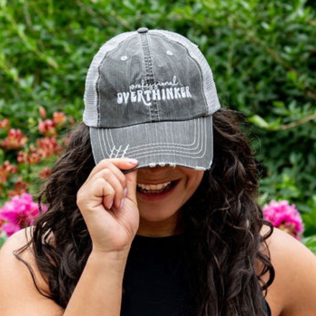 Female wearing a black washed trucker hat embroidered with professional overthinker.