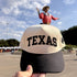 Texas Varsity trucker hat in Natural / Black Bill with raised black TEXAS block letters, held up at the State Fair of Texas