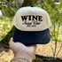 Wine Social Club trucker hat in Natural / Black Bill with black WINE Social Club EST.2025 lettering, held up outdoors