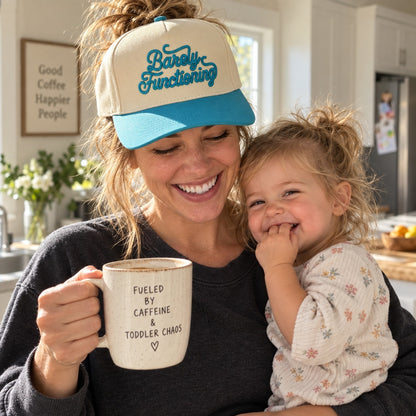 Mom holding coffee and a toddler wearing the Barely Functioning trucker hat in Natural / Aqua Bill