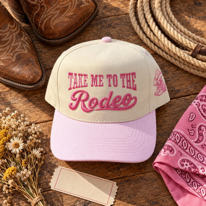 Take Me to the Rodeo trucker hat flat lay with cowboy boots, a lasso, a pink bandana, and dried wildflowers