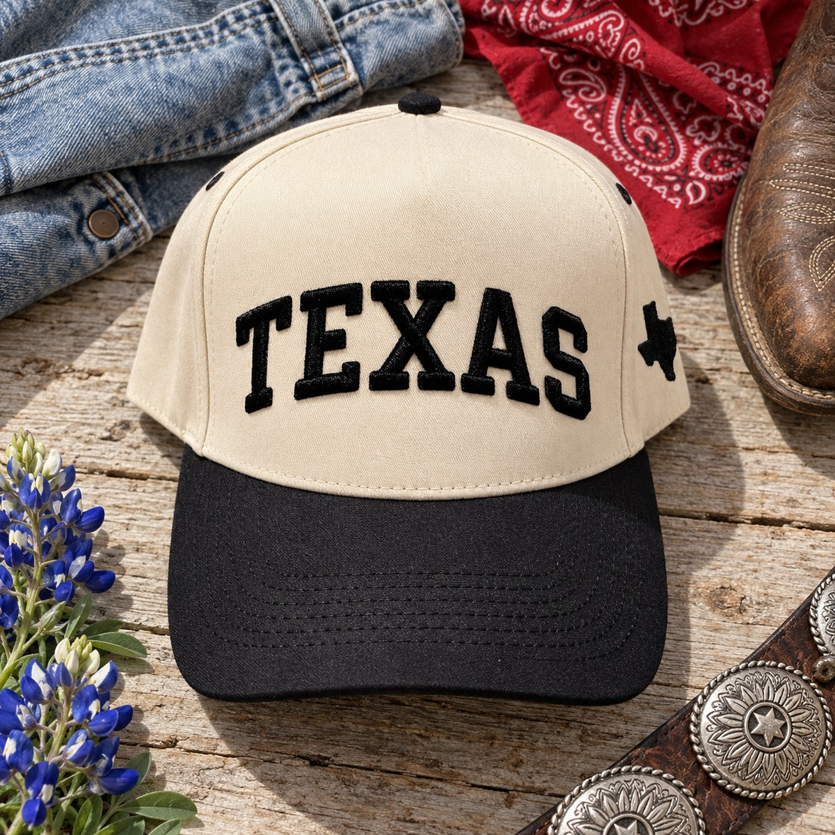 Texas Varsity trucker hat flat lay with a denim jacket, red bandana, cowboy boot, bluebonnets, and concho belt