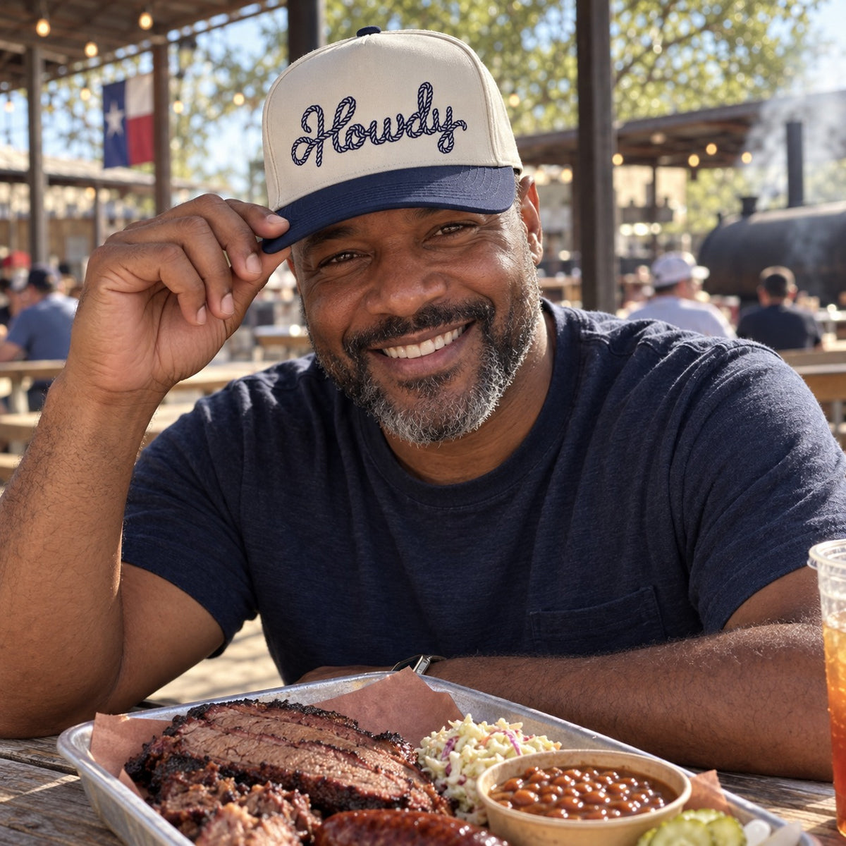 Man at a Texas barbecue picnic table wearing the Howdy Rope trucker hat in Natural / Navy Blue Bill with navy embroidery