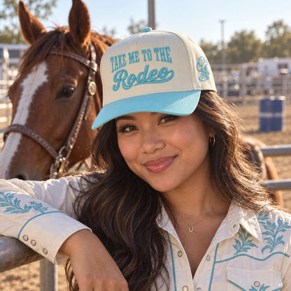 Woman at a barrel-racing pen wearing the Take Me to the Rodeo trucker hat in Natural / Aqua Bill with aqua embroidery