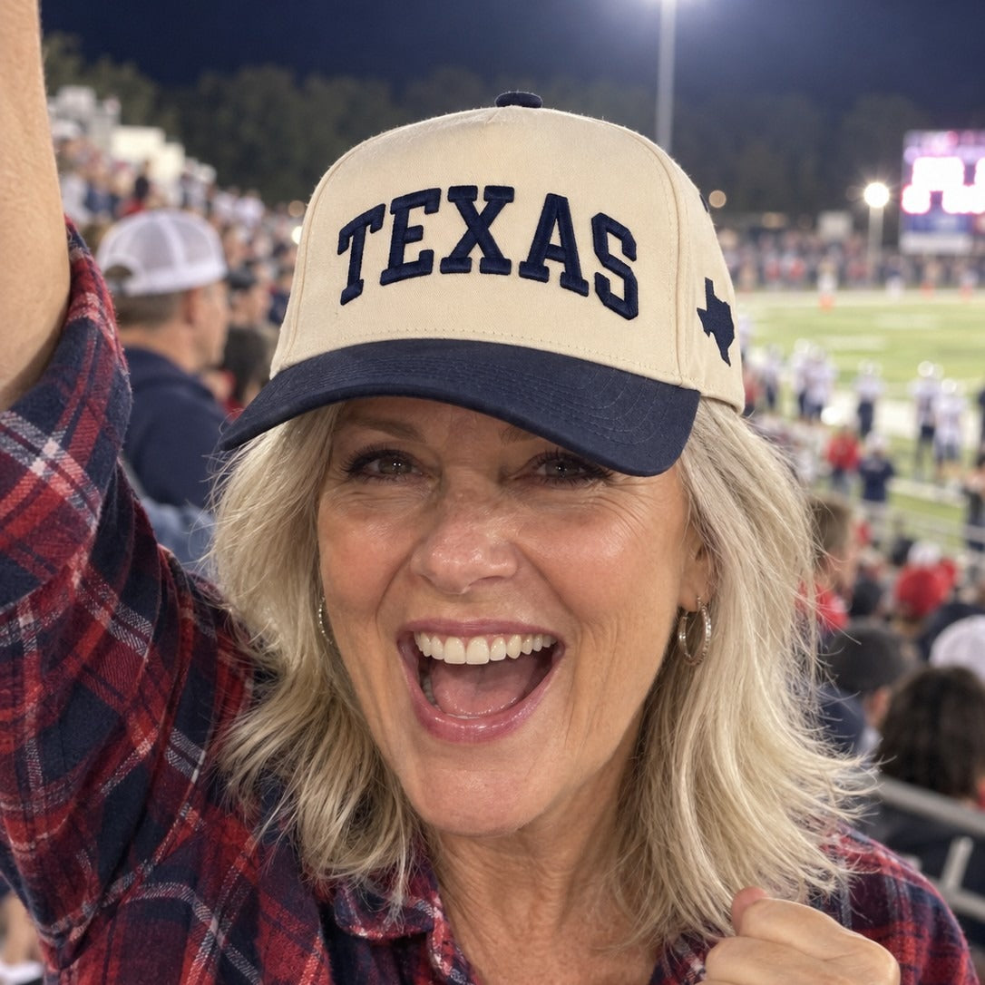 Woman cheering at a Friday night football game in the Texas Varsity trucker hat in Natural / Navy Blue Bill with navy embroidery