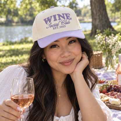 Woman at a picnic with rosé wearing the Wine Social Club trucker hat in Natural / Lavender Bill with lavender embroidery
