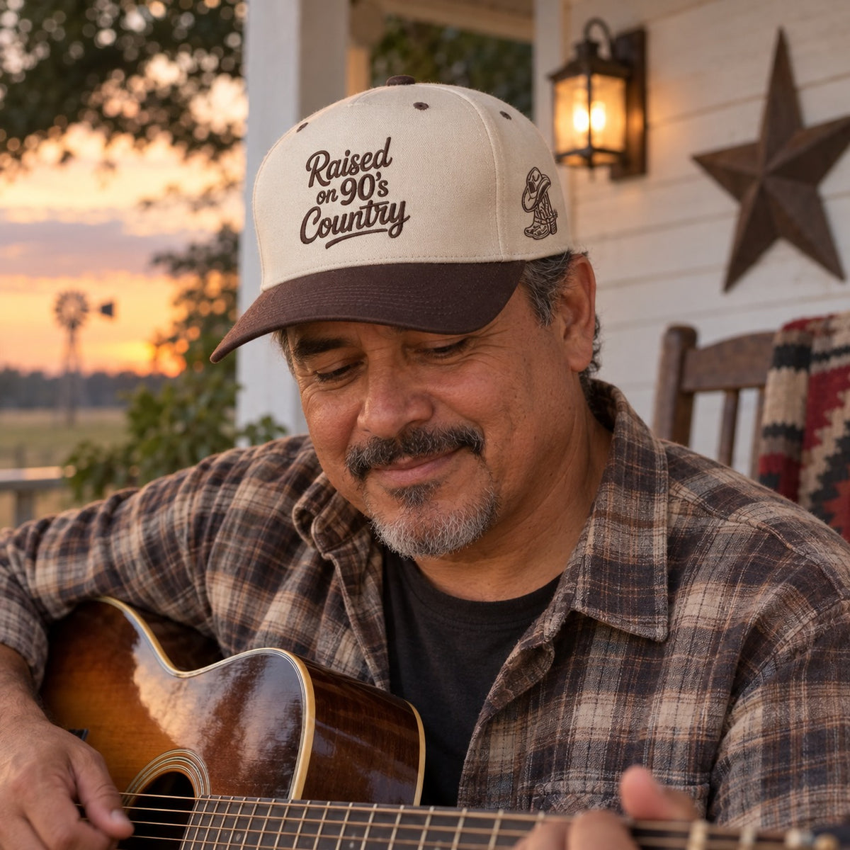 Man playing guitar on a farmhouse porch wearing the Raised on 90&