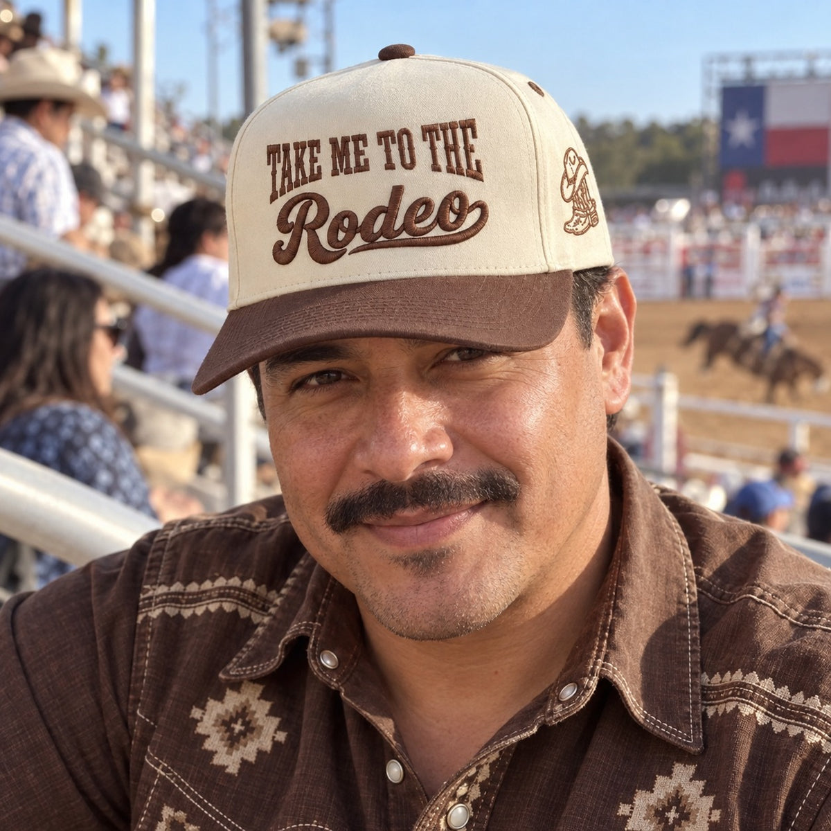 Man in rodeo bleachers wearing the Take Me to the Rodeo trucker hat in Natural / Brown Bill with brown embroidery