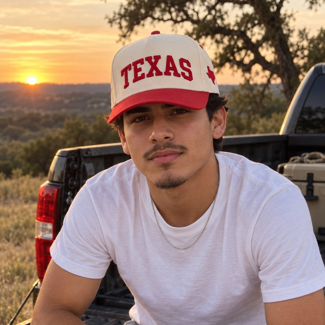 Man on a pickup tailgate in the Texas Hill Country wearing the Texas Varsity trucker hat in Natural / Red Bill with red embroidery