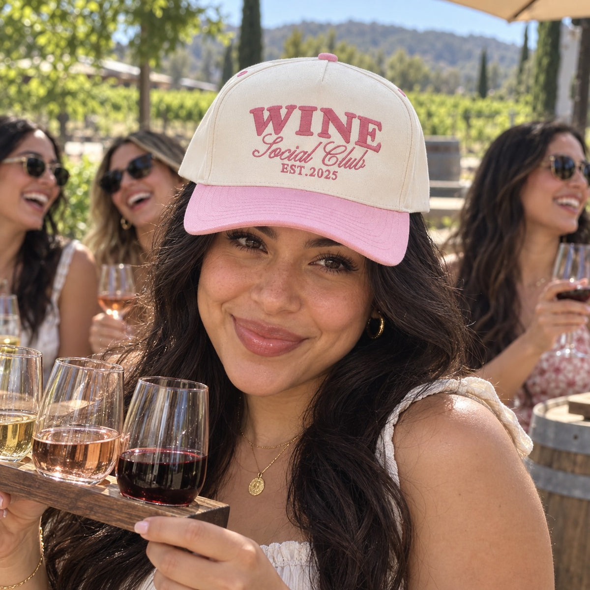 Woman on a winery tour with a wine flight wearing the Wine Social Club trucker hat in Natural / Pink Bill with pink embroidery