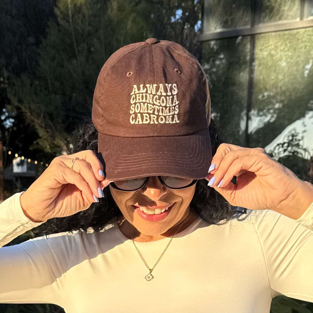 Woman wearing a brown baseball hat embroidered with Always Chingona Sometimes Cabrona Baseball hat