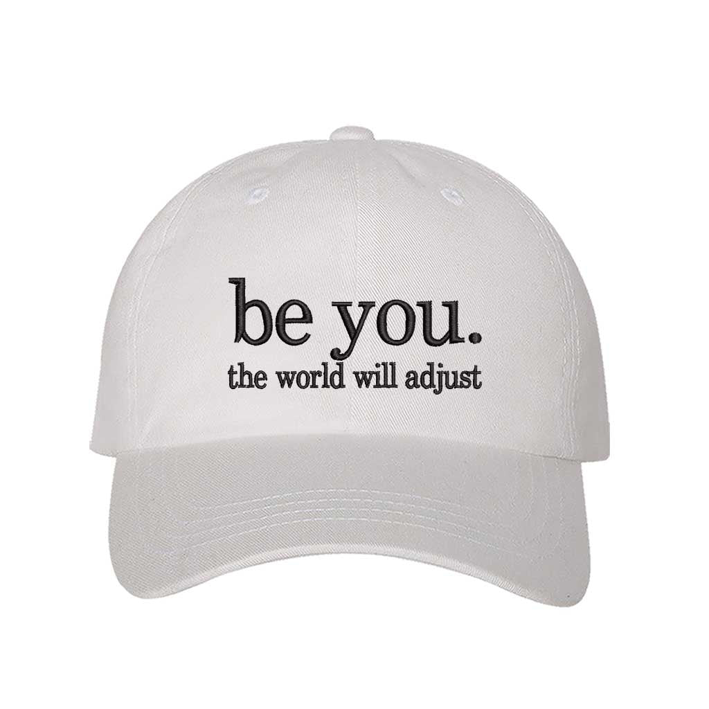 White Be You The World Will Adjust embroidered baseball hat featuring clean minimalist typography and professional stitching by DSY Lifestyle.