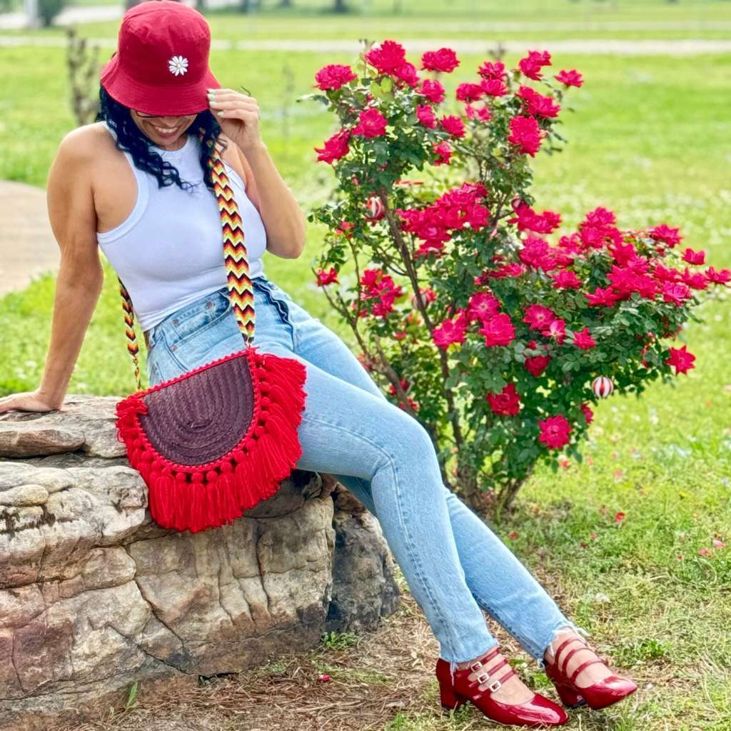 Woman sitting on a rock with bucket hat and aBurgundy Empanada Palm Purse with red tassels - DSY Lifestyle