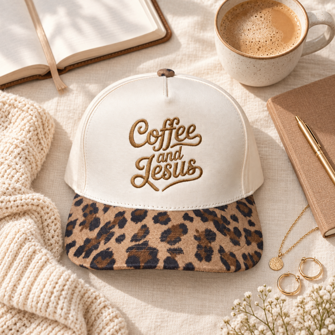 A baseball cap styled in a cozy flat-lay arrangement on a cream fabric surface. The cap has an off-white crown with gold embroidered text reading &
