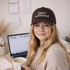 A close-up view of a female wearing DSY Lifestyle brown cotton baseball hat featuring the phrase Highly Caffeinated in bold, crisp white embroidery. - DSY Lifestyle