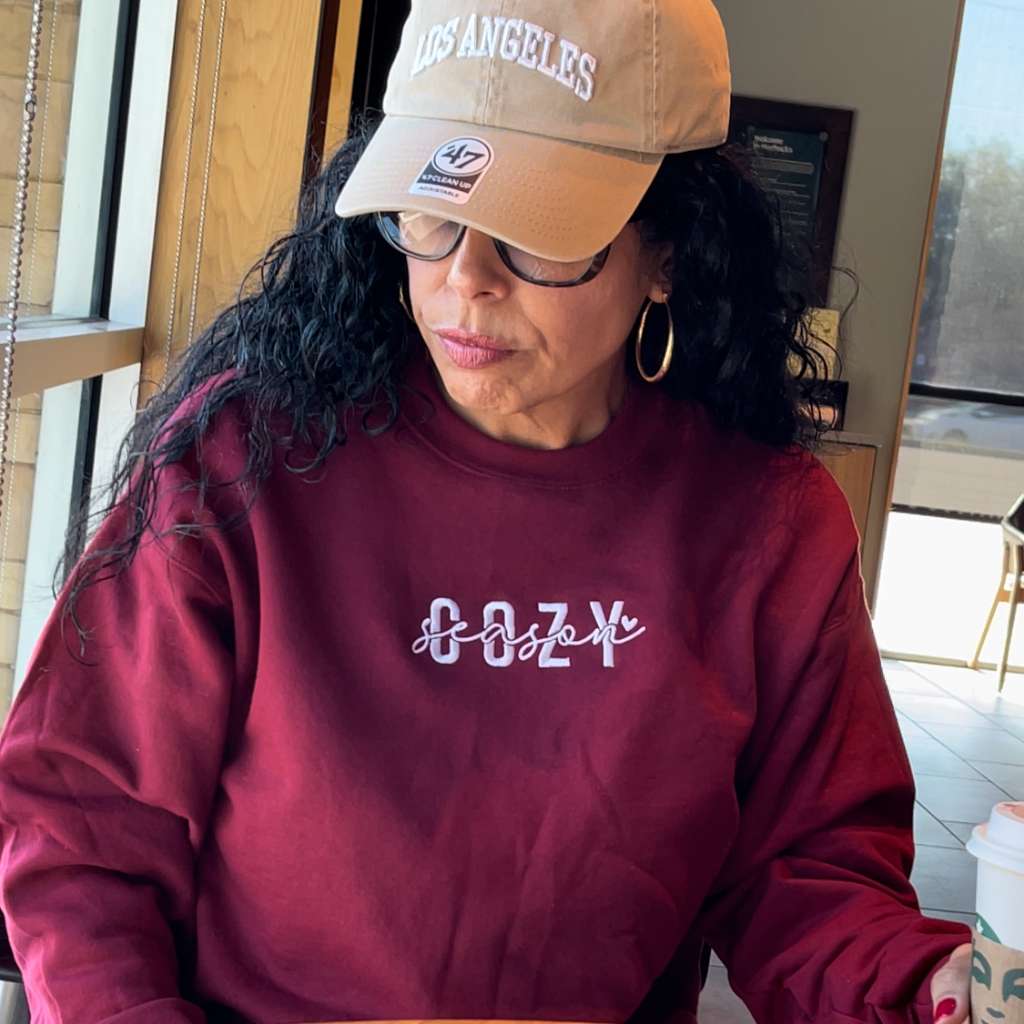 Female wearing a burgundy crewneck sweatshirt embroidered with Cozy Season - DSY Lifestyle