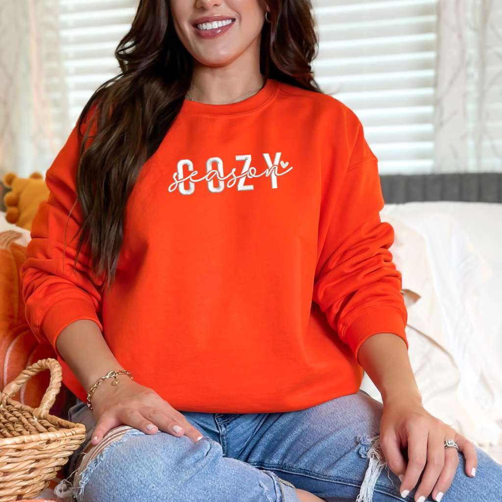Female wearing a orange crewneck sweatshirt embroidered with Cozy Season - DSY Lifestyle