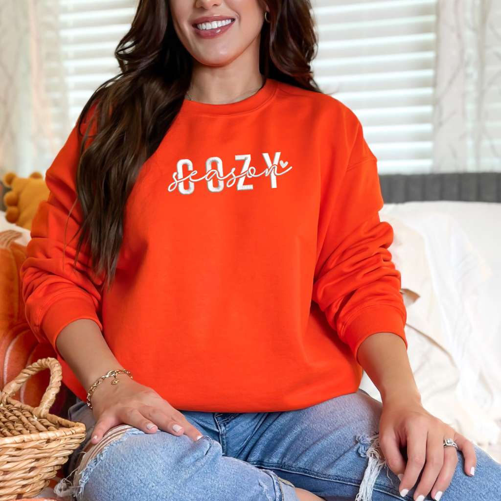 Female wearing a orange crewneck sweatshirt embroidered with Cozy Season - DSY Lifestyle