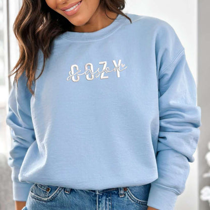 Female wearing a light blue crewneck sweatshirt embroidered with Cozy Season - DSY Lifestyle