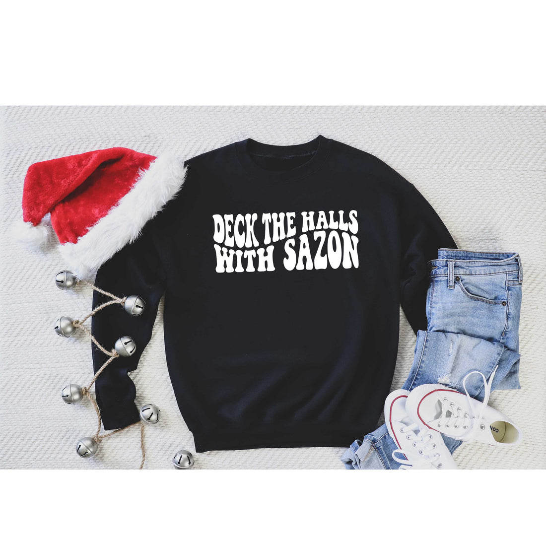 Flat lay of Deck the Halls with Sazón Black sweatshirt, cozy holiday sweater with Latin flair, styled with seasonal accents