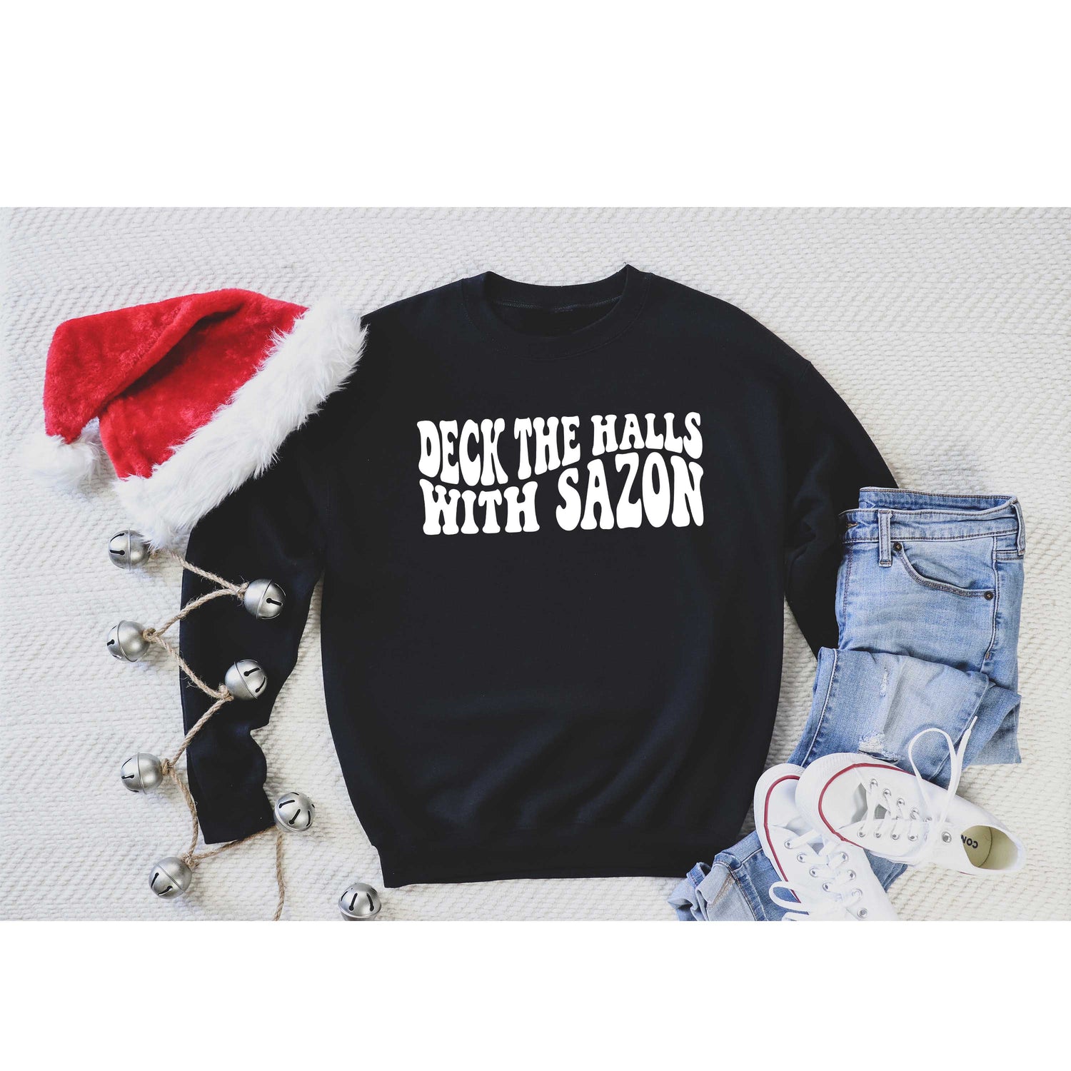 Flat lay of Deck the Halls with Sazón Black sweatshirt, cozy holiday sweater with Latin flair, styled with seasonal accents