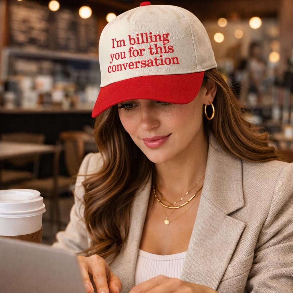 Woman wearing a cap with text, sitting at a table in a cafe.
