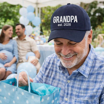 Handsome grandpa with gift bag wearing a Navy Blue Grandpa Est. 2026 Baseball Hat featuring bold white embroidery on a premium dad cap; a stylish 2026 announcement gift for new grandfathers by DSY Lifestyle.