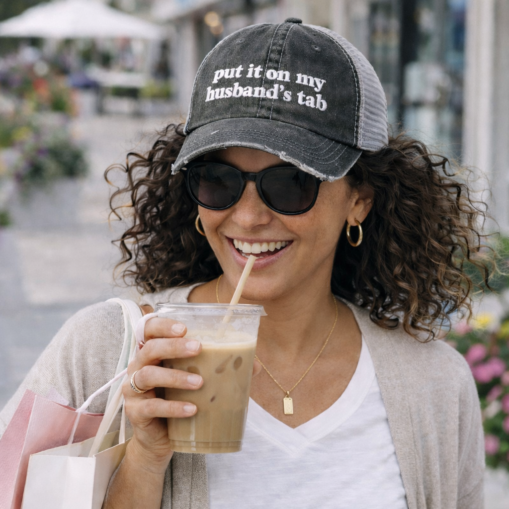 Female with iced coffee in hand wearing Black DSY Lifestyle distressed trucker hat featuring the words Put It On My Husband&