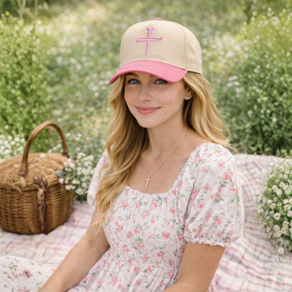 Female sitting in park on a blanket wearing a Natural Pink Nail Cross 3D Puff Two-Tone Baseball Hat featuring a raised nail cross on a structured natural crown with a contrasting visor; a premium faith statement by DSY Lifestyle.