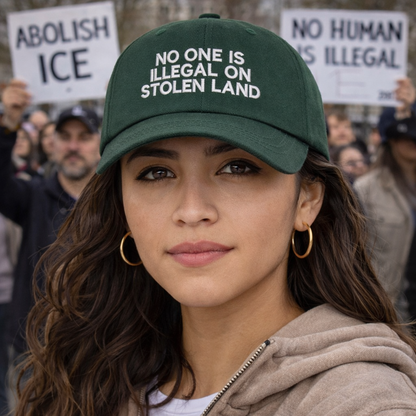 Female protestor with powerful message wearing a Forest Green No One Is Illegal On Stolen Land Baseball Hat featuring bold white embroidery on a classic cotton dad cap; a powerful social justice statement piece by DSY Lifestyle.