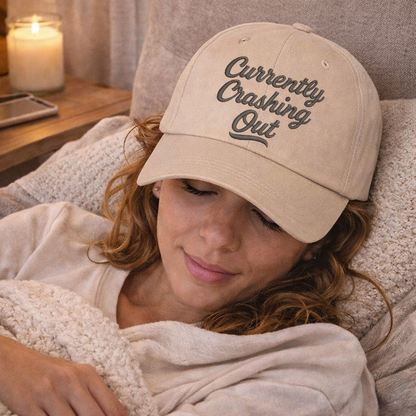 Female relaxing nap with cozy essentials wearing a Stone Currently Crashing Out embroidered baseball hat. A statement baseball hat for women who love humor, comfort, and effortless everyday outfits. - DSY Lifestyle